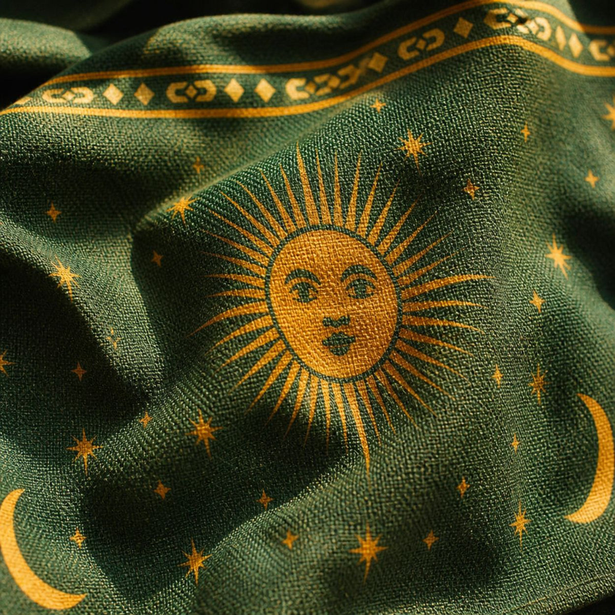 Close-up of the Astra print — golden sun face and stars woven on deep green