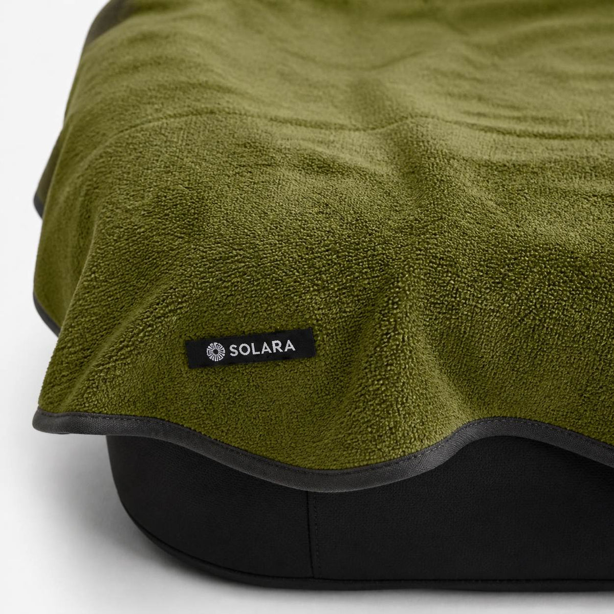 Close-up of the Solara label and bound edge on the Oliva olive green car seat towel