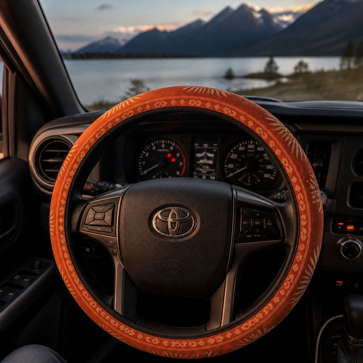 Sol steering wheel cover by Solara on the wheel at dusk, lake and mountain view