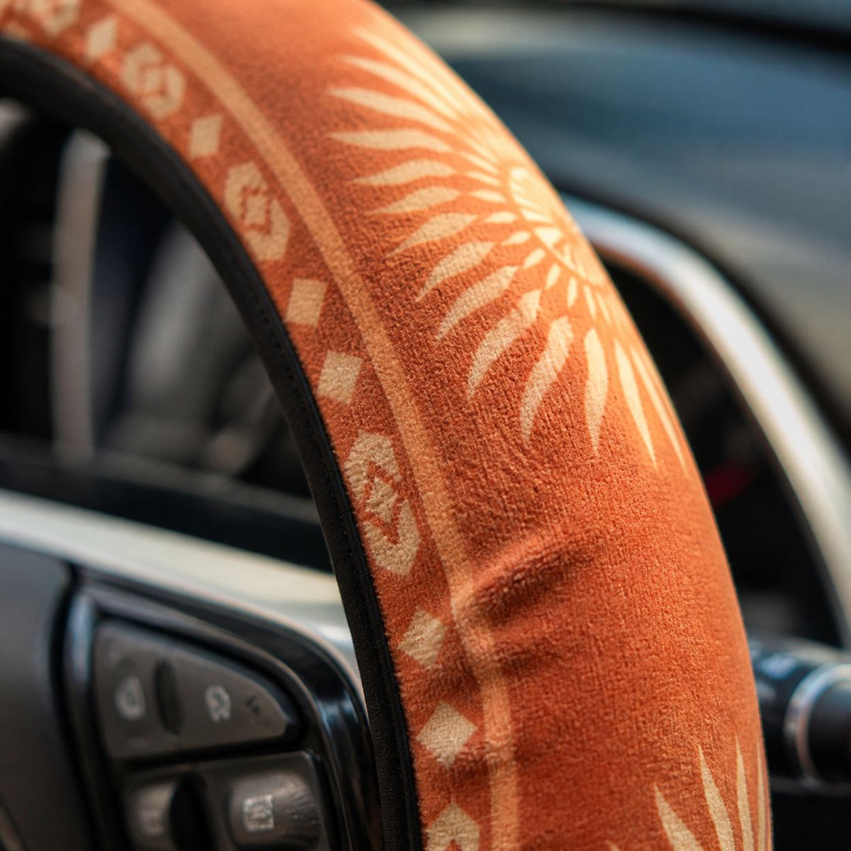 Close-up of the soft faux suede on the Sol steering wheel cover by Solara, warm orange sunburst print