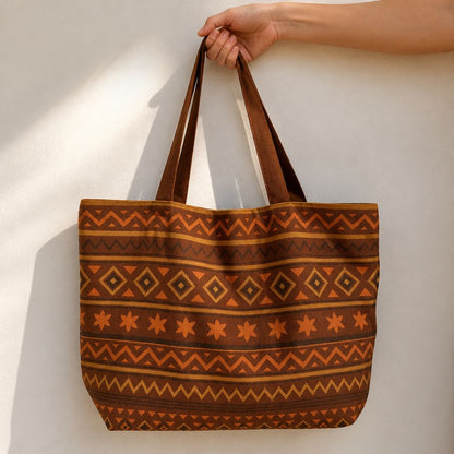 Savana tote bag in tan cotton canvas with burgundy and navy Aztec diamond pattern, held against a sunlit cream wall