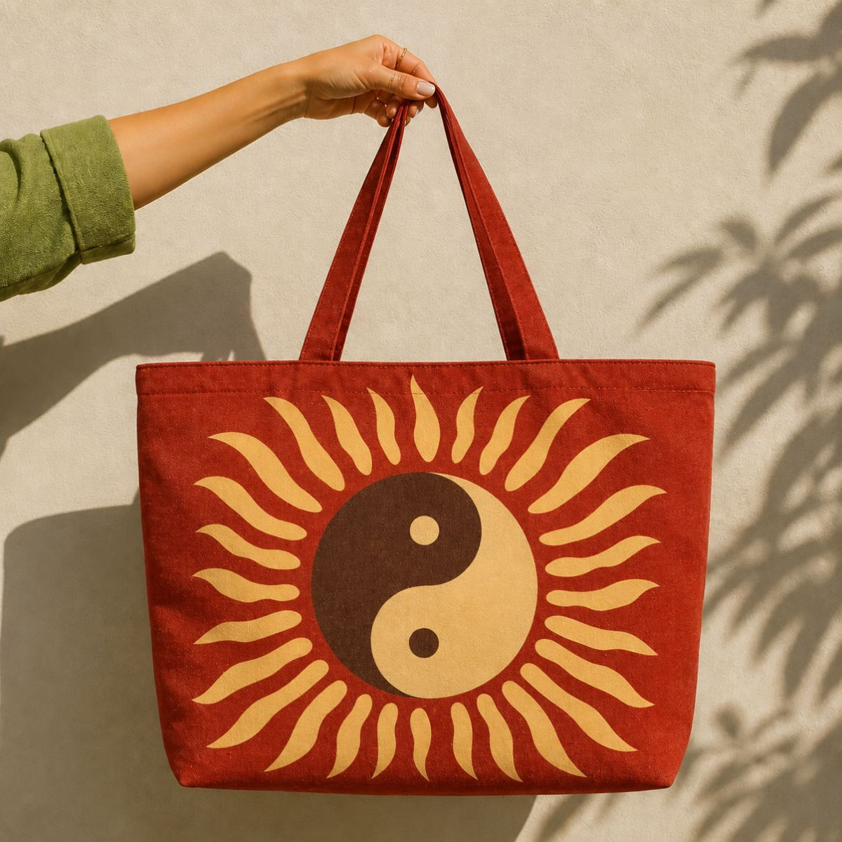 Tao tote bag held against a sunlit wall — golden yin-yang sun on rust red canvas