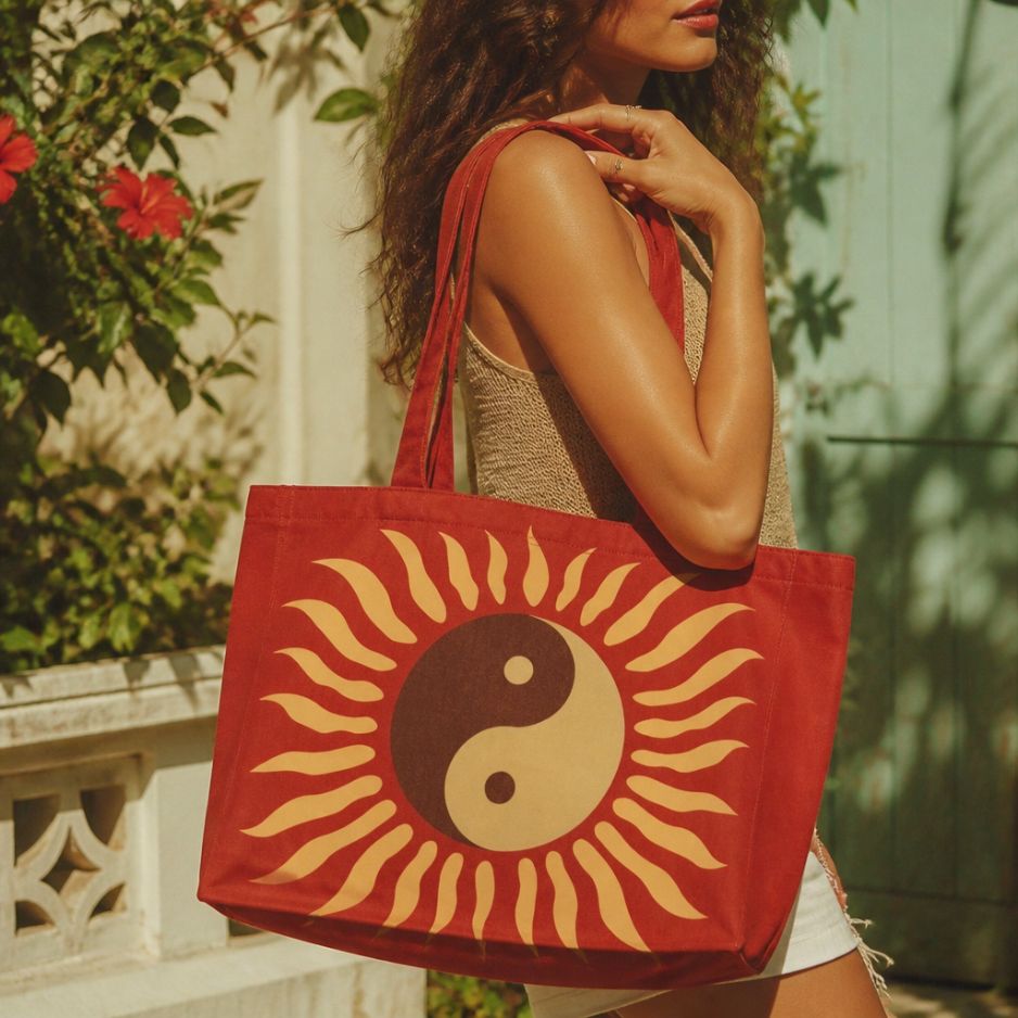 Tao rust-red tote bag carried over the shoulder in a garden courtyard