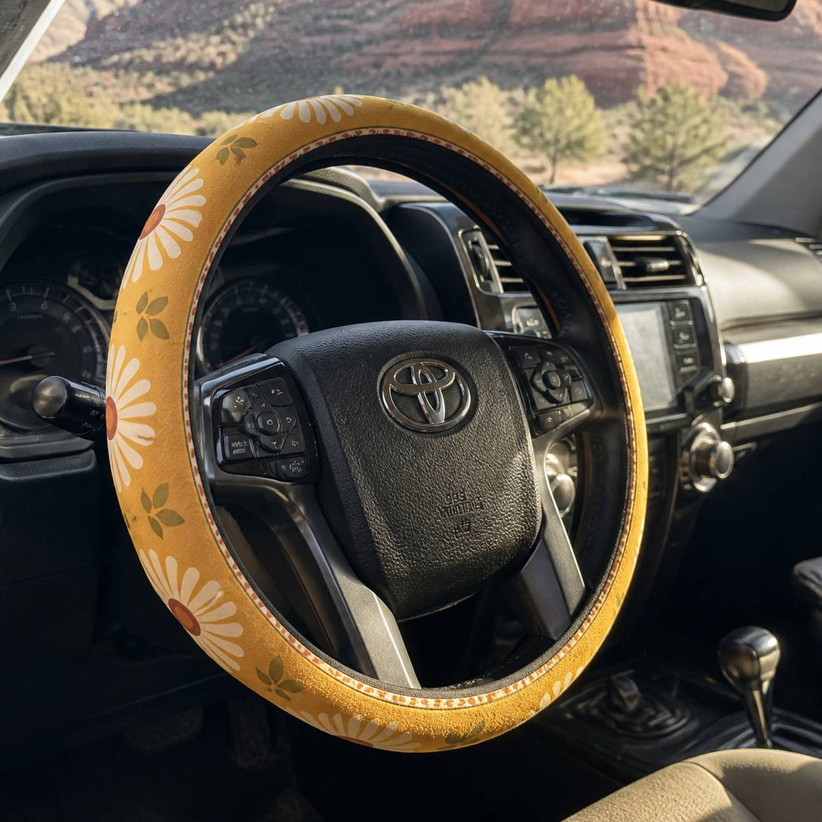 Daisy steering wheel cover by Solara, seen from the passenger side: mustard and cream daisy print