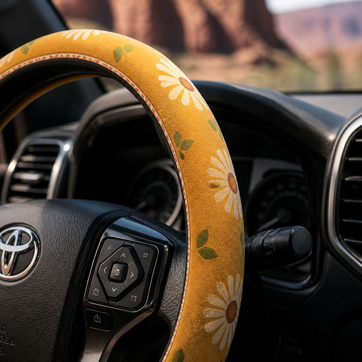 Close-up of the Daisy steering wheel cover by Solara on the rim by the spoke, mustard and cream daisy print