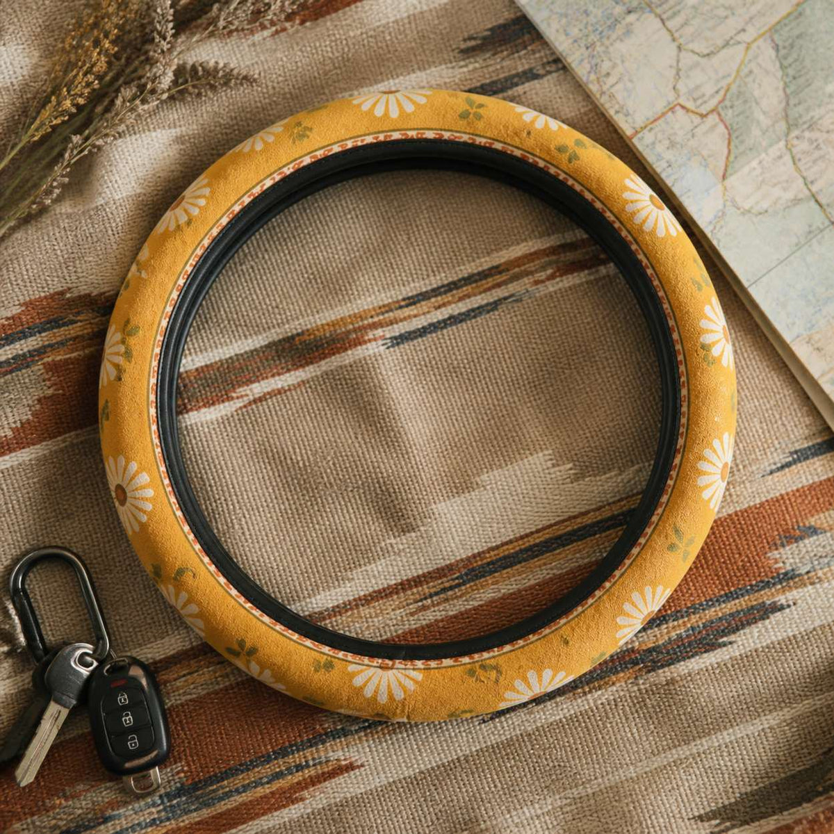 Daisy steering wheel cover by Solara on a woven blanket next to car keys, mustard and cream daisy print