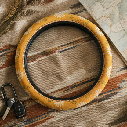 Daisy steering wheel cover by Solara on a woven blanket next to car keys, mustard and cream daisy print