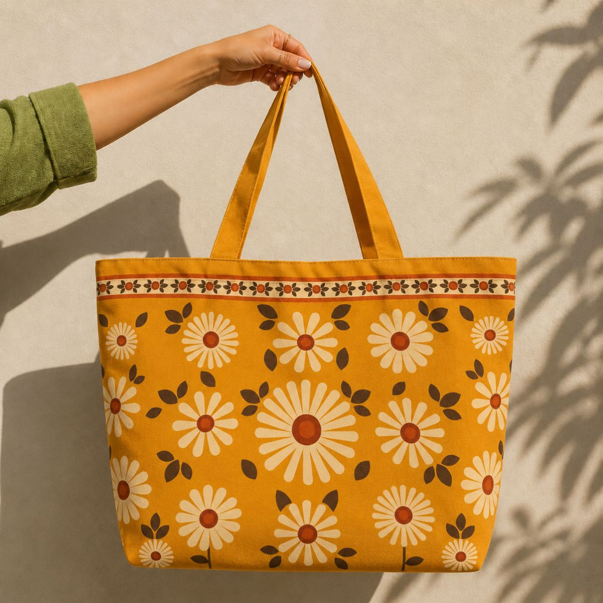 Daisy tote bag held up against a sunlit cream wall — retro white daisies on mustard cotton canvas
