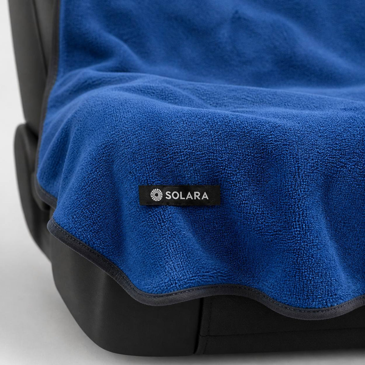Close-up of the Solara label and bound edge on the Marina blue car seat towel