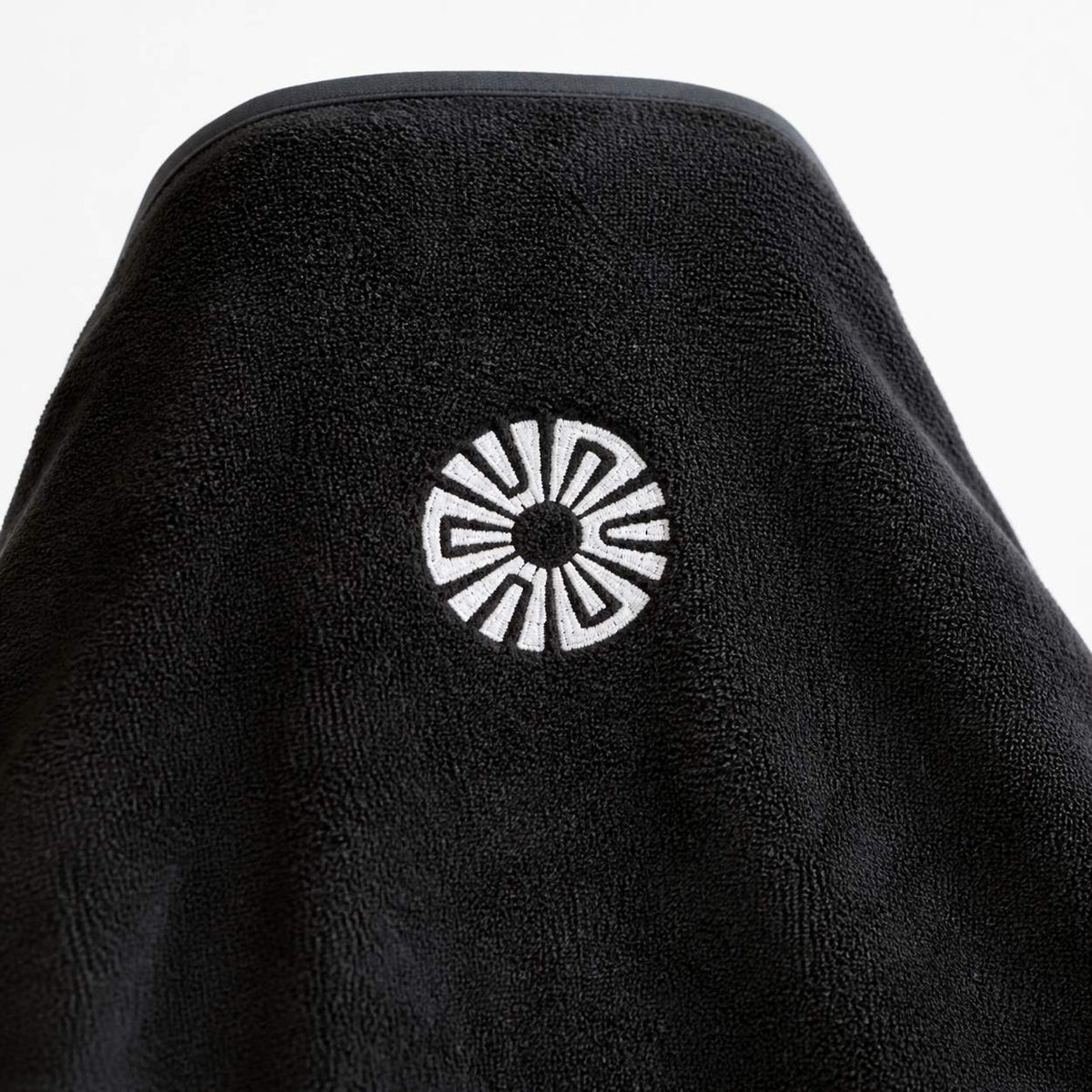 Close-up of the embroidered Solara sun logo on the hood of the Noche black car seat towel