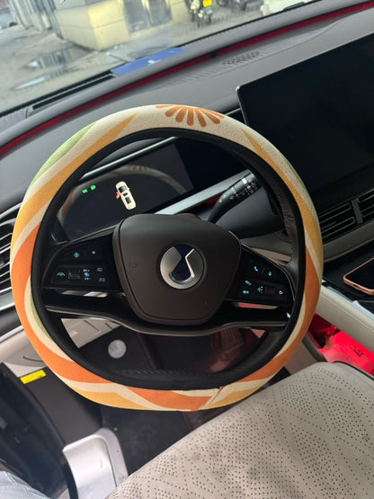 Ripple steering wheel cover by Solara — tangerine, mustard, olive and cream wave print fitted on a car steering wheel