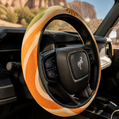 Close-up of the Ripple steering wheel cover by Solara on the rim by the spoke, tangerine, mustard, olive and cream wave print