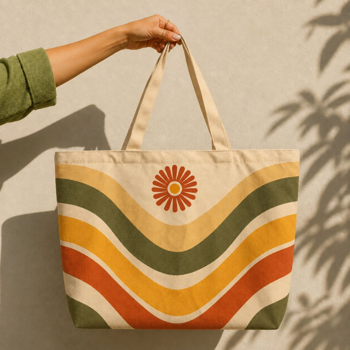 Ripple tote bag held against a sunlit wall — retro waves in olive, marigold and rust with a daisy medallion