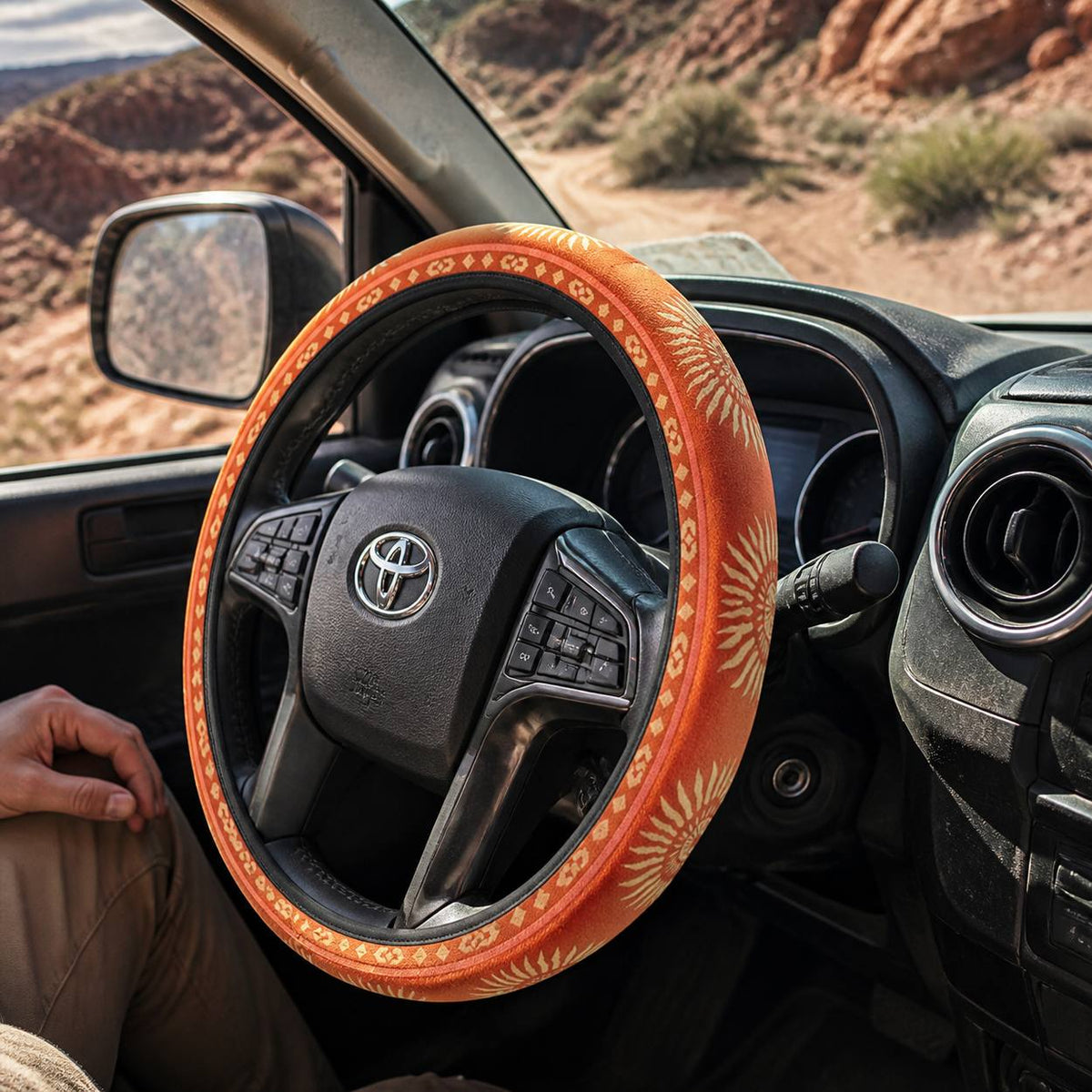 Sol steering wheel cover by Solara, seen from the passenger side: warm orange sunburst print