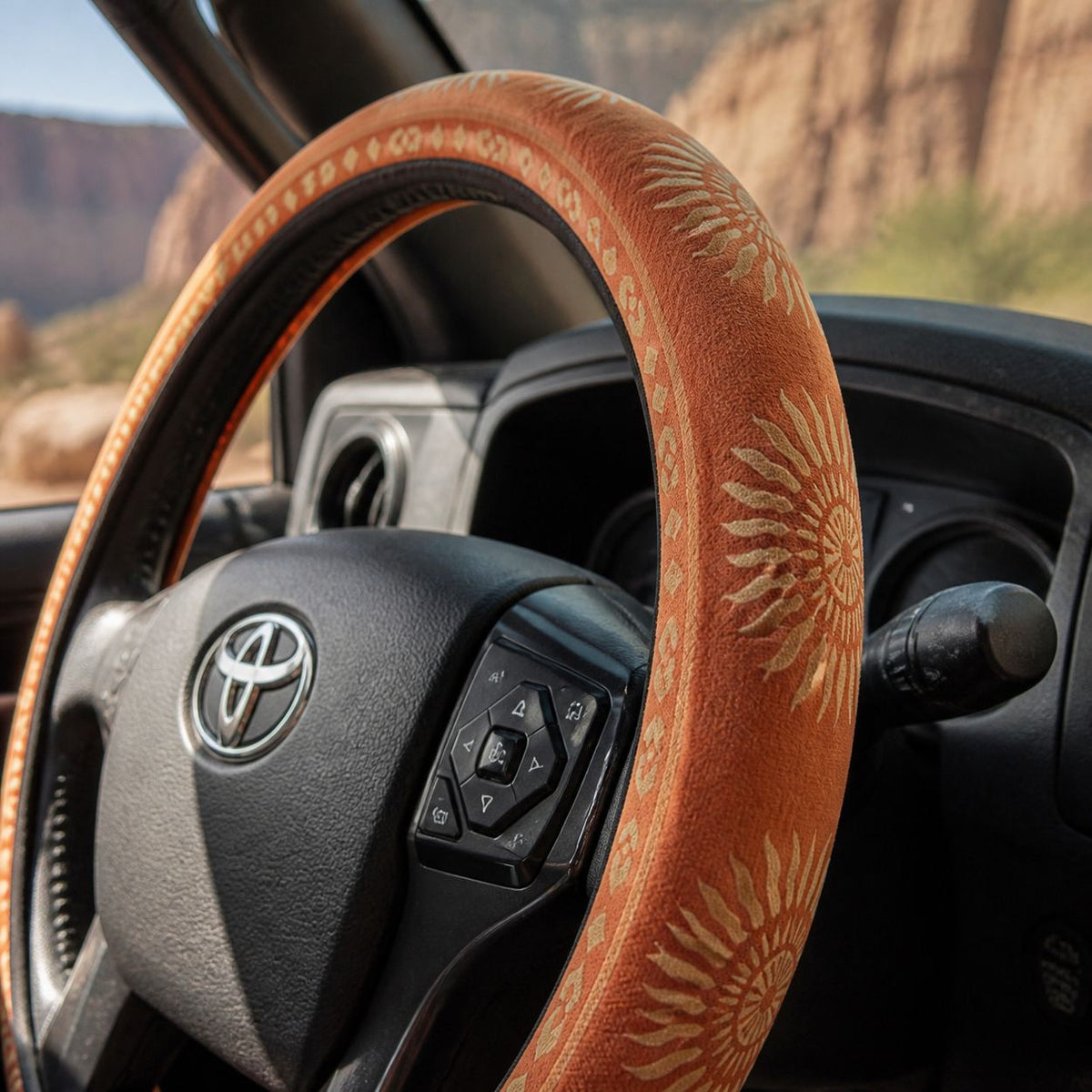 Close-up of the Sol steering wheel cover by Solara on the rim by the spoke, warm orange sunburst print