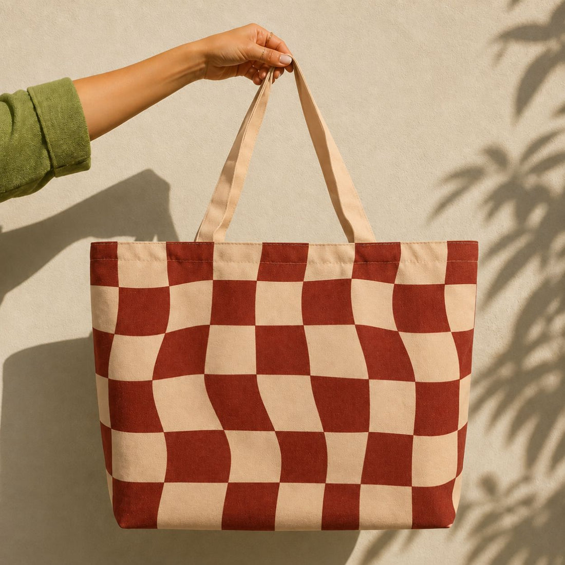Terra tote bag held against a sunlit wall — hand-warped brick-red checkerboard on cream